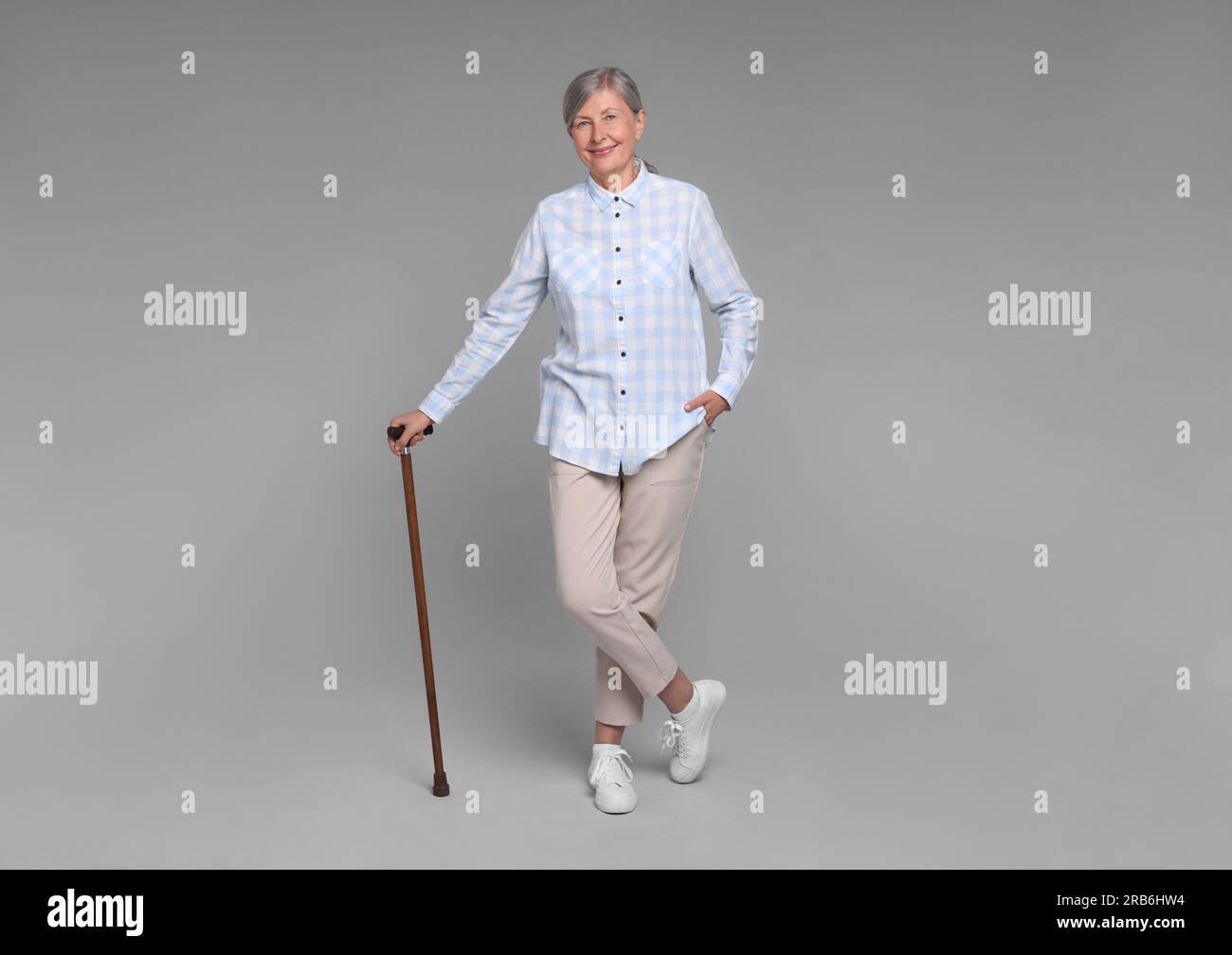 Senior woman with walking cane on gray background Stock Photo - Alamy