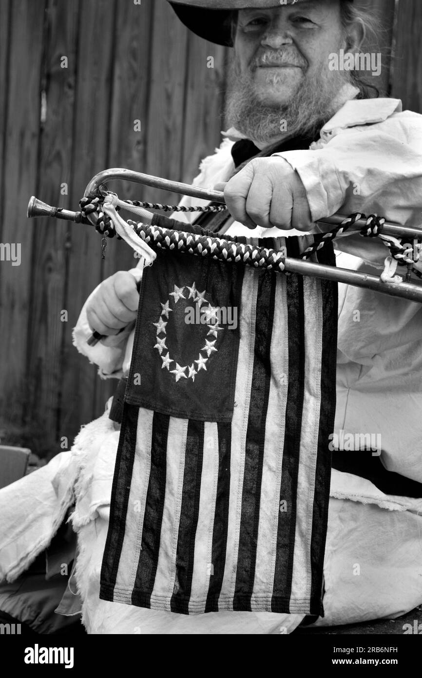 An American history reenactor plays and holds a trumpet embellished with a US flag with 13 stars at a living history event in Abingdon, Virginia. Stock Photo