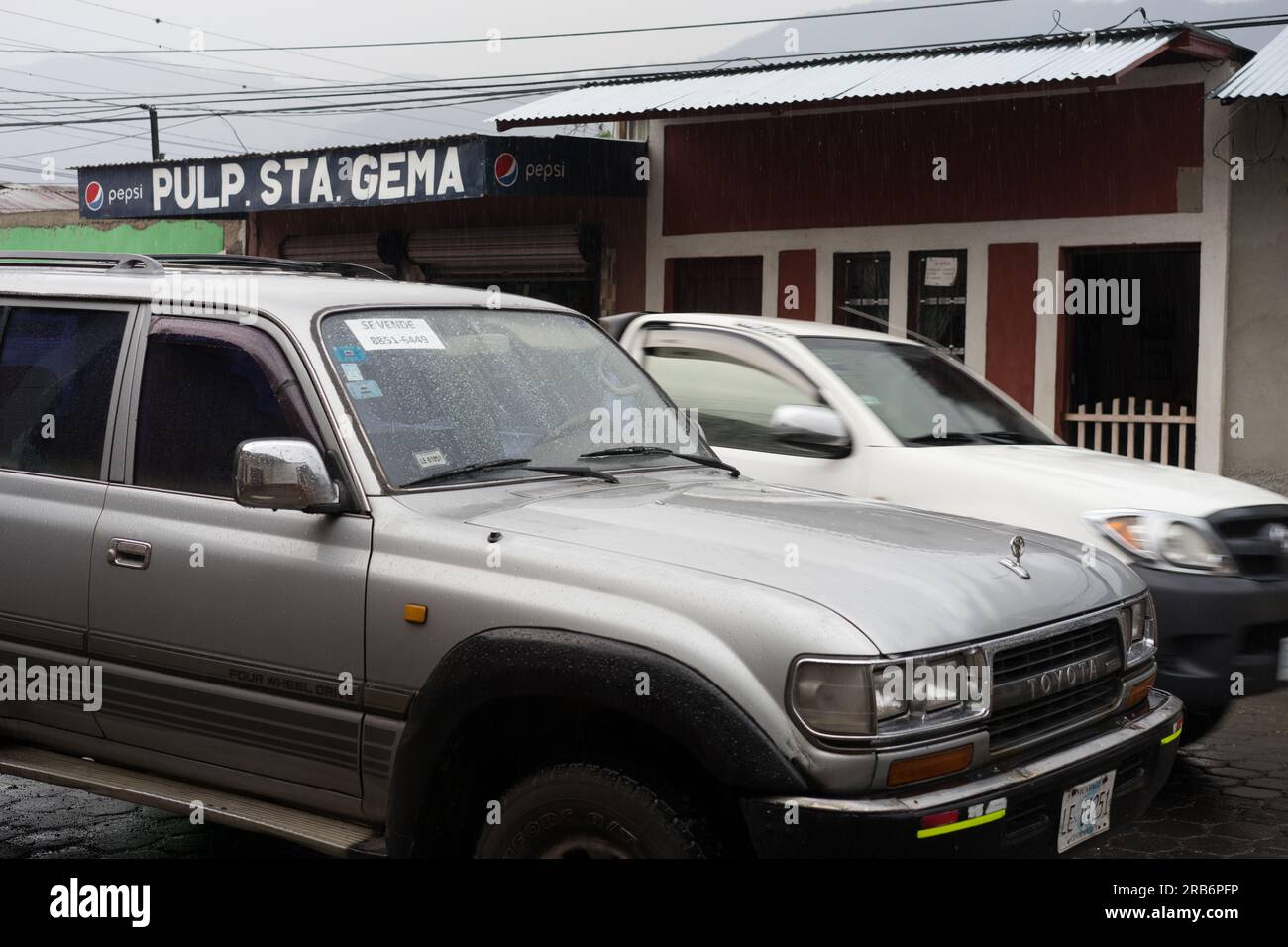 Toyota SUV parked on street as a white pickup truck passes on a street in Jinotega, Nicaragua.  Toyotas are quite common in Nicaragua. Stock Photo