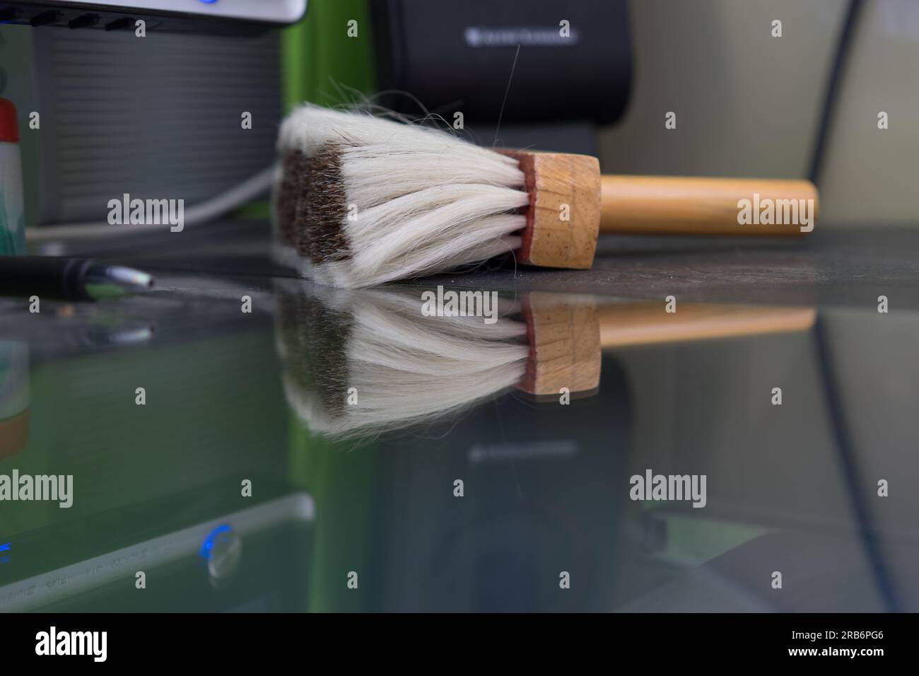 https://c8.alamy.com/comp/2RB6PG6/white-dusting-brush-with-dark-inner-bristles-and-its-reflection-on-a-glass-topped-computer-table-2RB6PG6.jpg