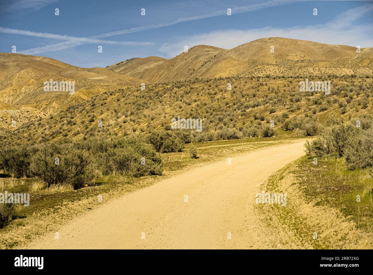 Curved dirt road goes through desert hills under blue sky. Stock Photo