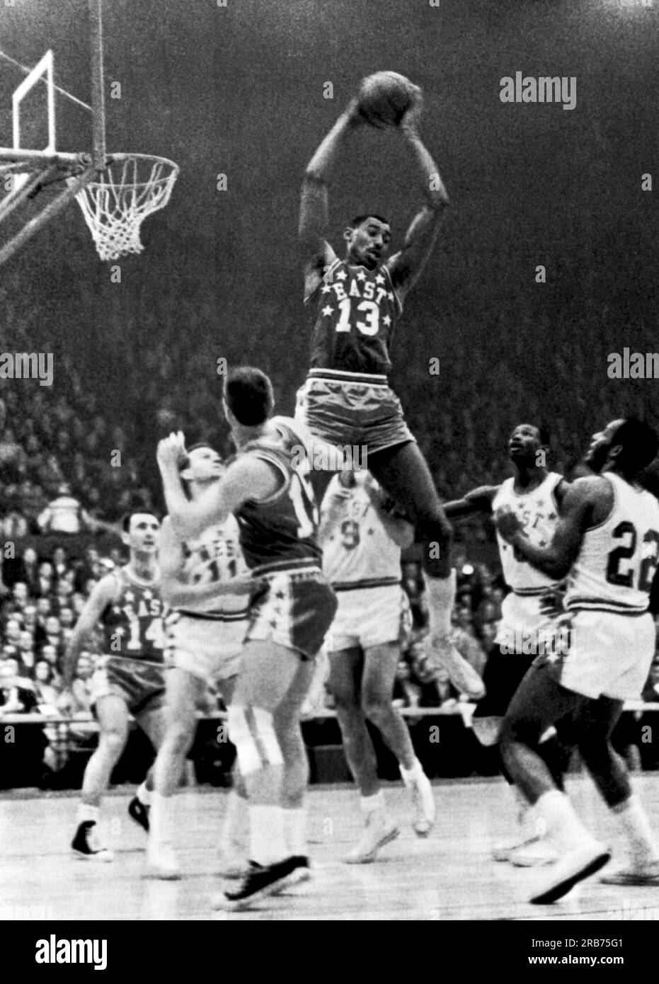 St. Louis, Missouri:  January 16, 1962 Wilt Chamberlain, Philadelphia (13), goes up high to snag a rebound in the NBA All-Star game. Below him are (l-r) Bob Cousy, Boston (14); Jerry West, Los Angeles (11); Tom Heinsohn,  Boston (15); Bob Pettit, St. Louis (9); Walt Bellamy, Chicago (8) and Elgin Baylor, Los Angeles (22). Stock Photo