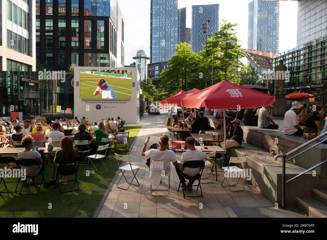 Tony Wilson place. Crowd watching Wimbledon tennis match on screen. People sat at tables eating and drinking. Manchester UK. Stock Photo