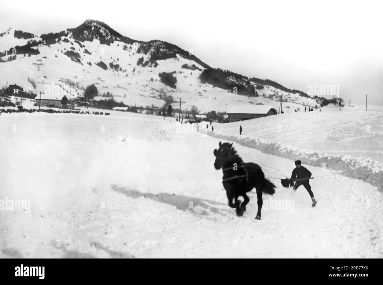 Adelboden, Switzerland:  1927 A skier enjoying the sport of skijoring behind a horse going up a hill in the Alps of Adelboden . Stock Photo