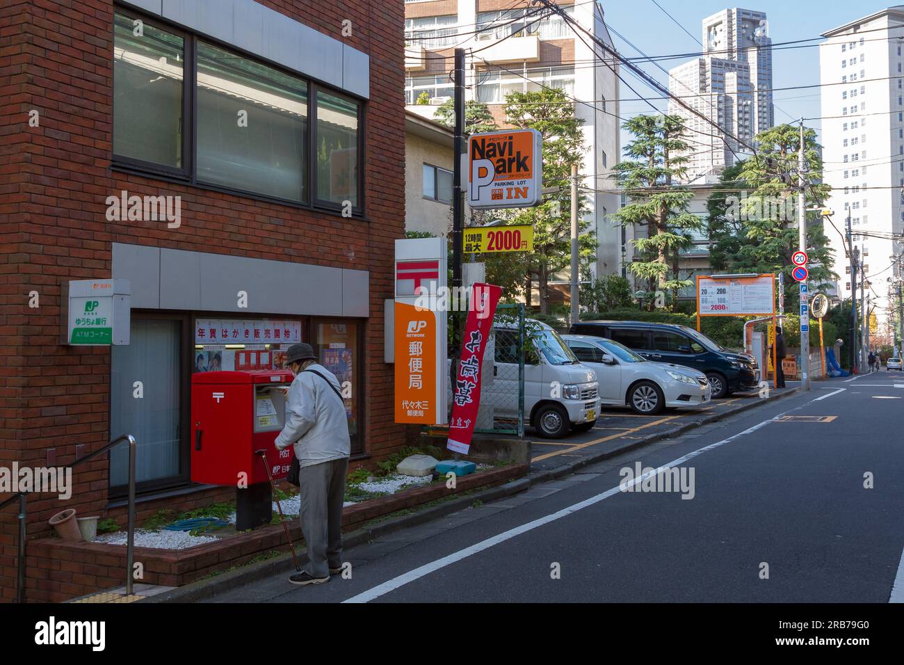 An older Japanese man post mail in a post box outside a small Post Office in Shinjuku, Tokyo, Japan. Stock Photo