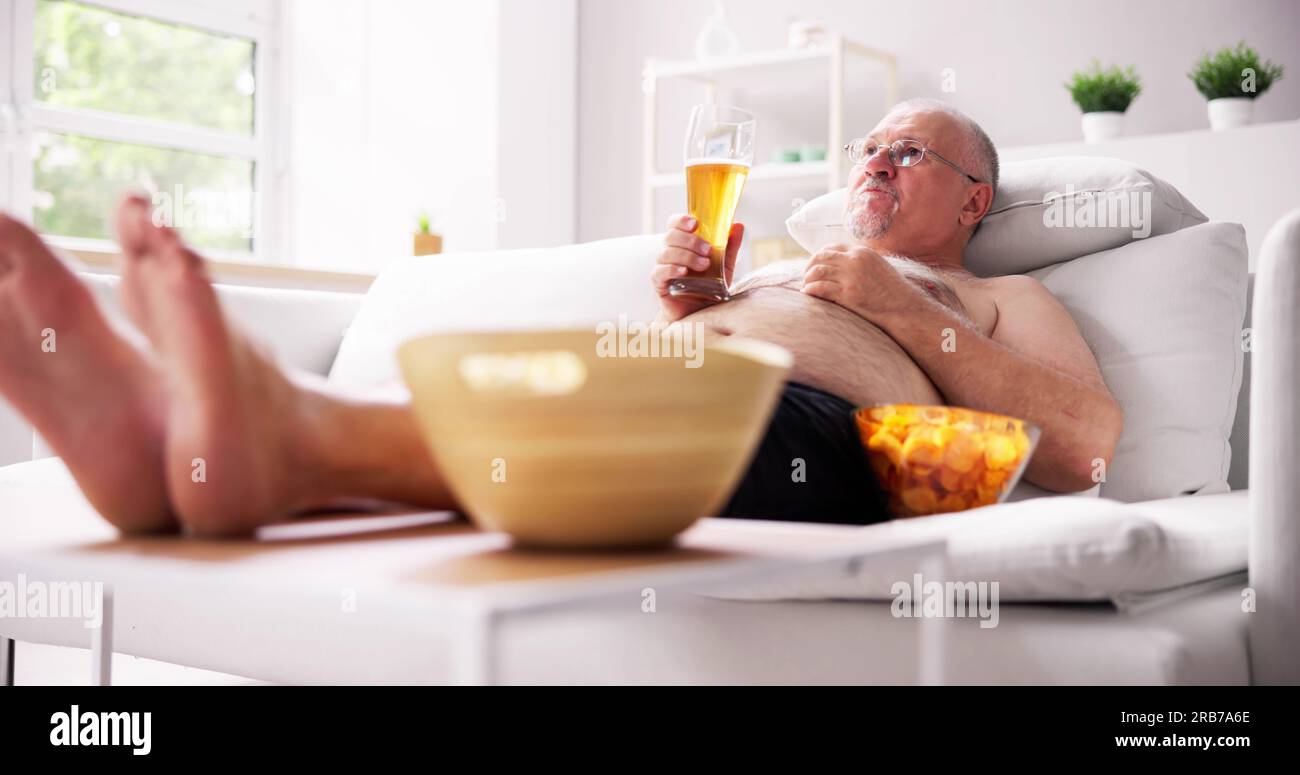 Overeating Junk Food, Drinking Beer And Watching TV Stock Photo