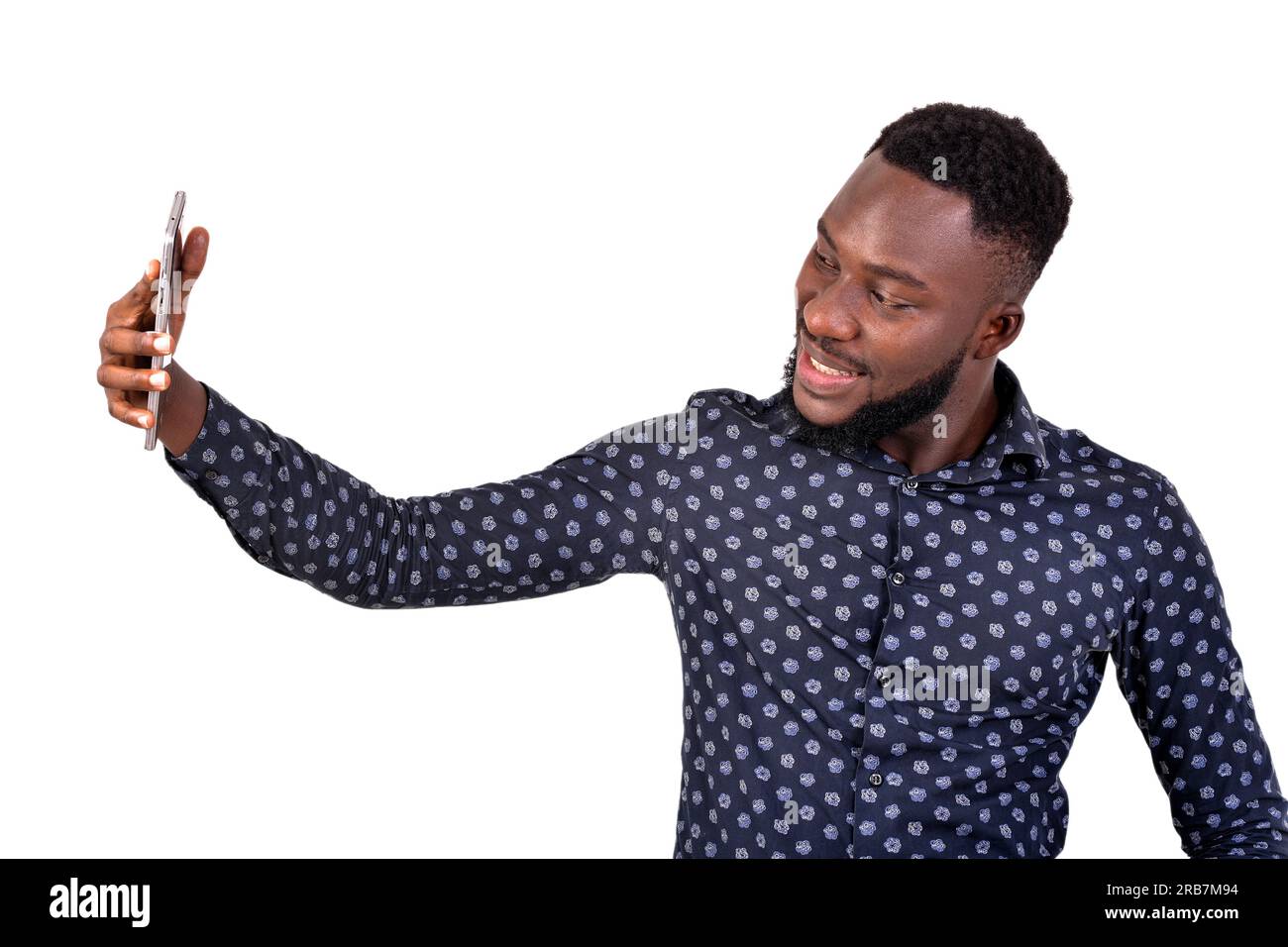 a young bearded man standing on a white background self-photographing using cell phone, smiling. Stock Photo