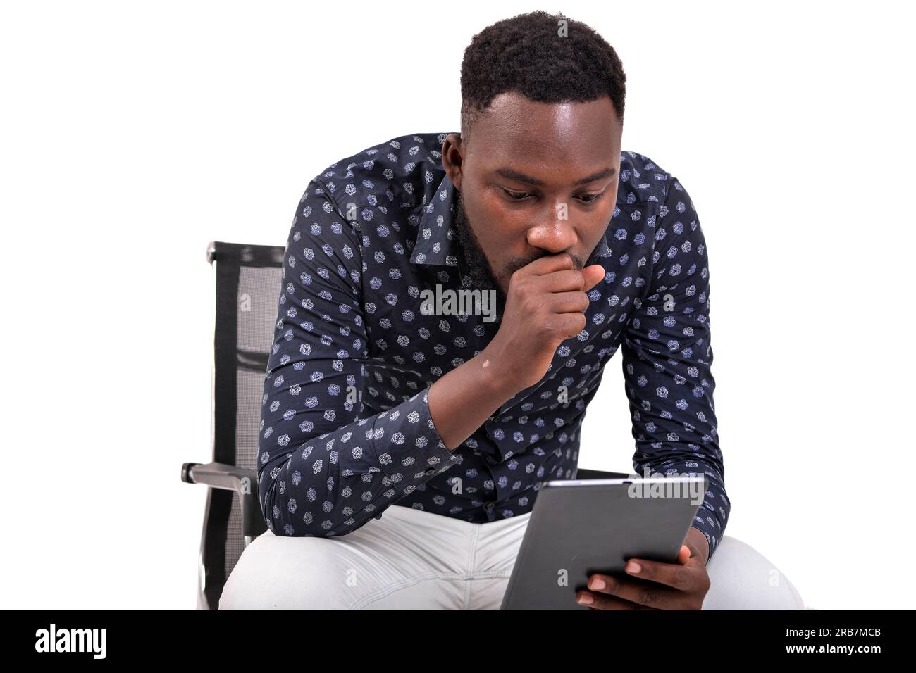 a young bearded man sitting against white background looking at tablet in amazement Stock Photo