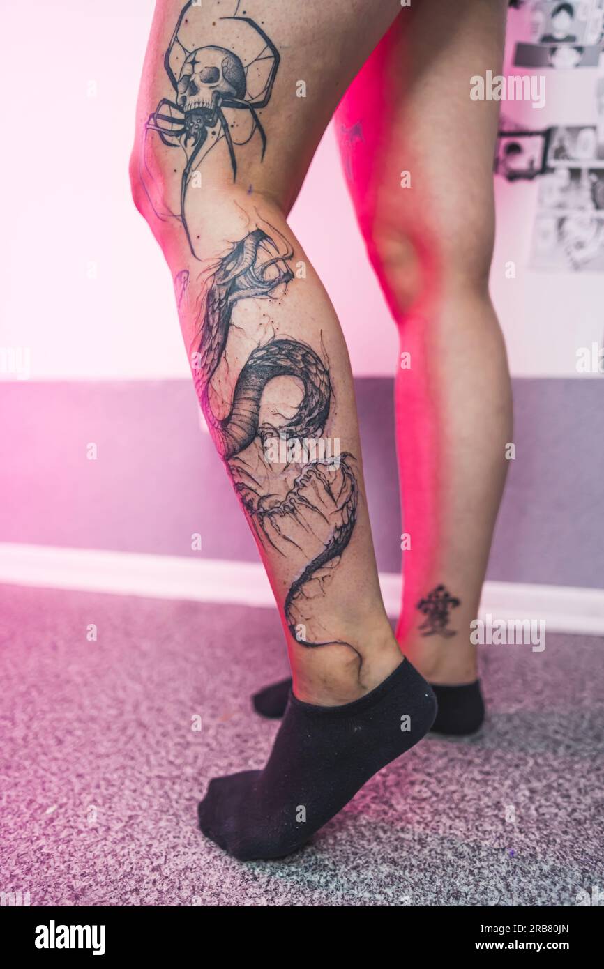 Professional black ink tattoos on a leg of a caucasian person. Spider, skull, and dragon tattoo. Indoor vertical shot. High quality photo Stock Photo