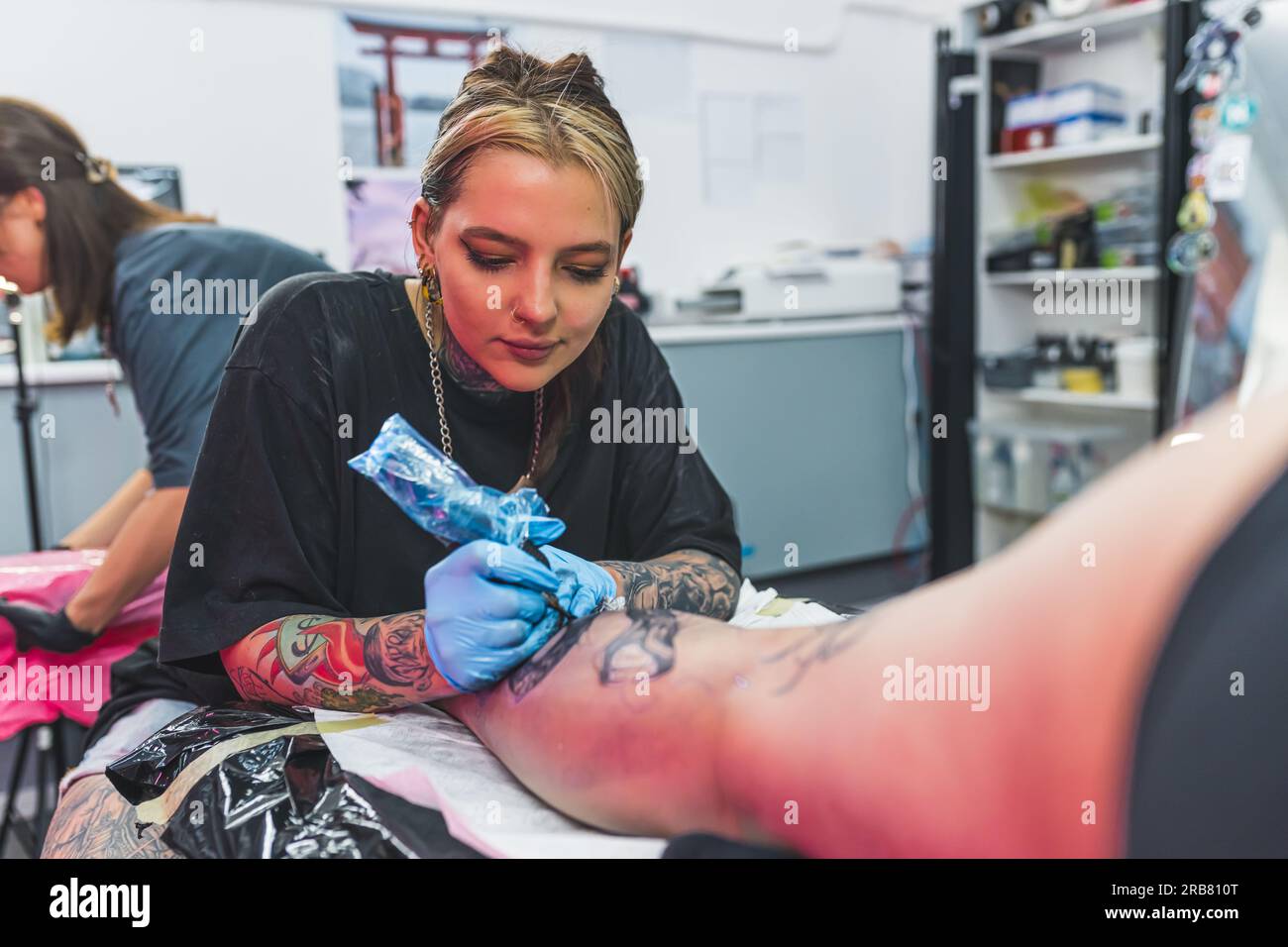 Focused young adult female tattooist drawing a tattoo on her client's leg. Blurred interior of a tattooing studio. High quality photo Stock Photo