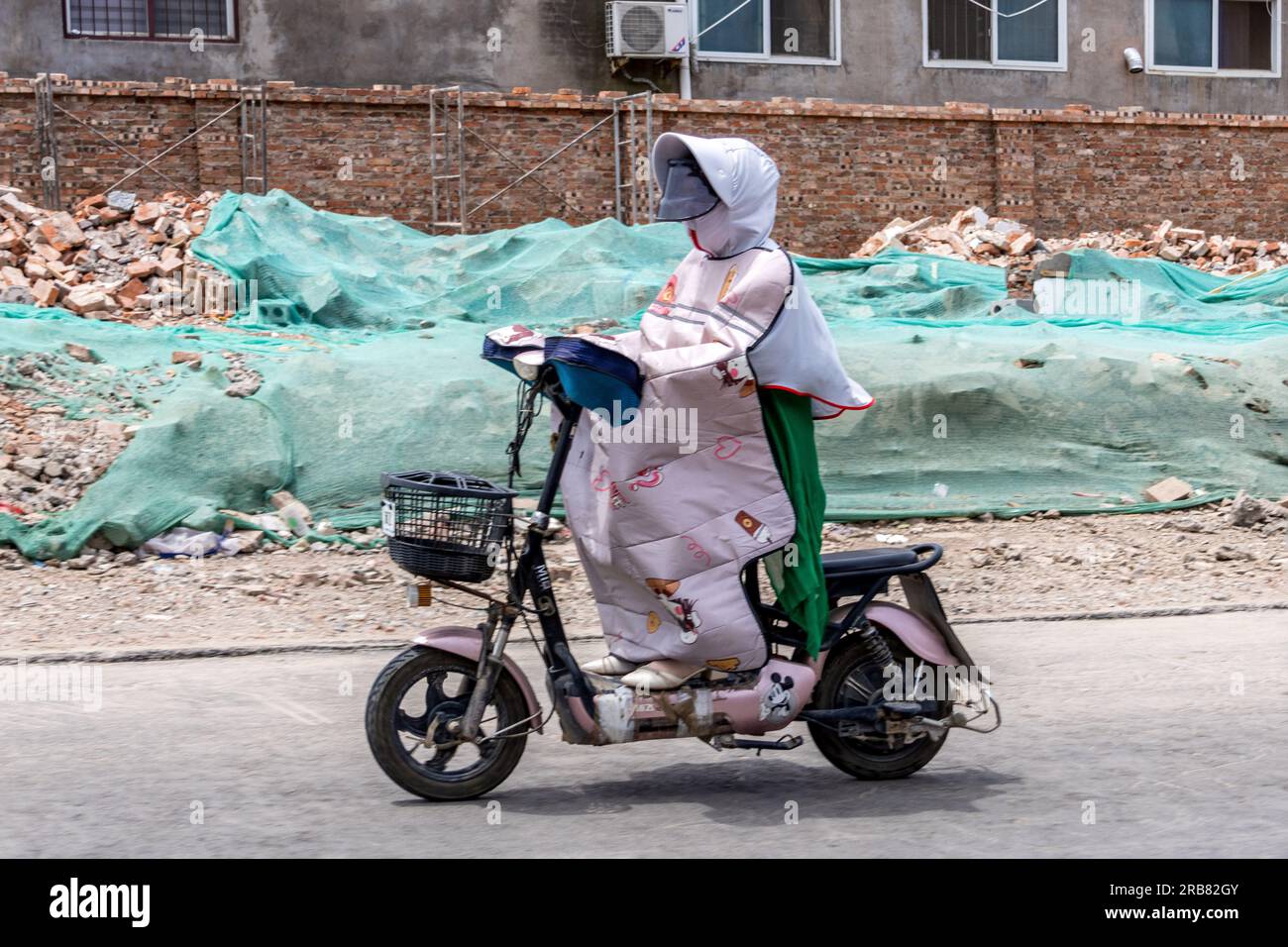 ANYANG, CHINA - JULY 8, 2023 - A pedestrian wearing protective clothing riding on a street in a temperature of 40 degrees Celsius in Hua County, Anyan Stock Photo