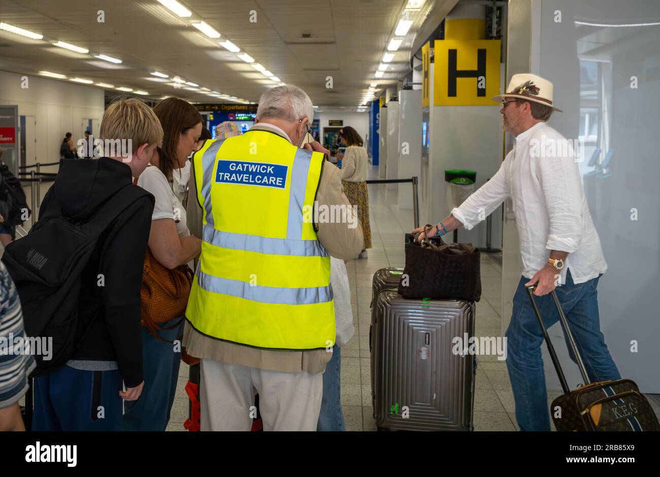 A volunteer with Gatwick Travelcare assists travellers at London Gatwick Airport South Terminal, West Sussex, UK. Gatwick Travelcare is staffed by vol Stock Photo