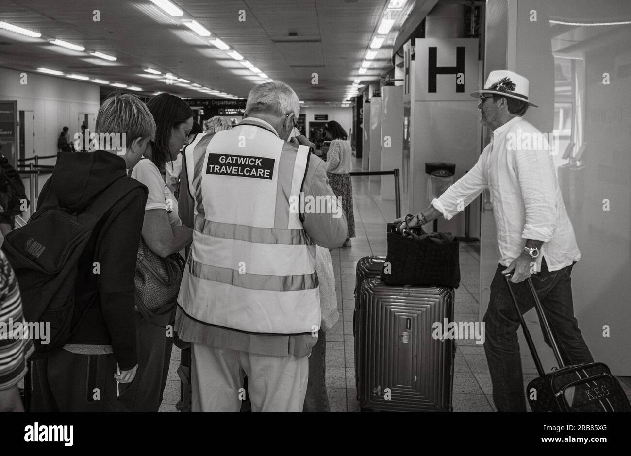 A volunteer with Gatwick Travelcare assists travellers at London Gatwick Airport South Terminal, West Sussex, UK. Gatwick Travelcare is staffed by vol Stock Photo