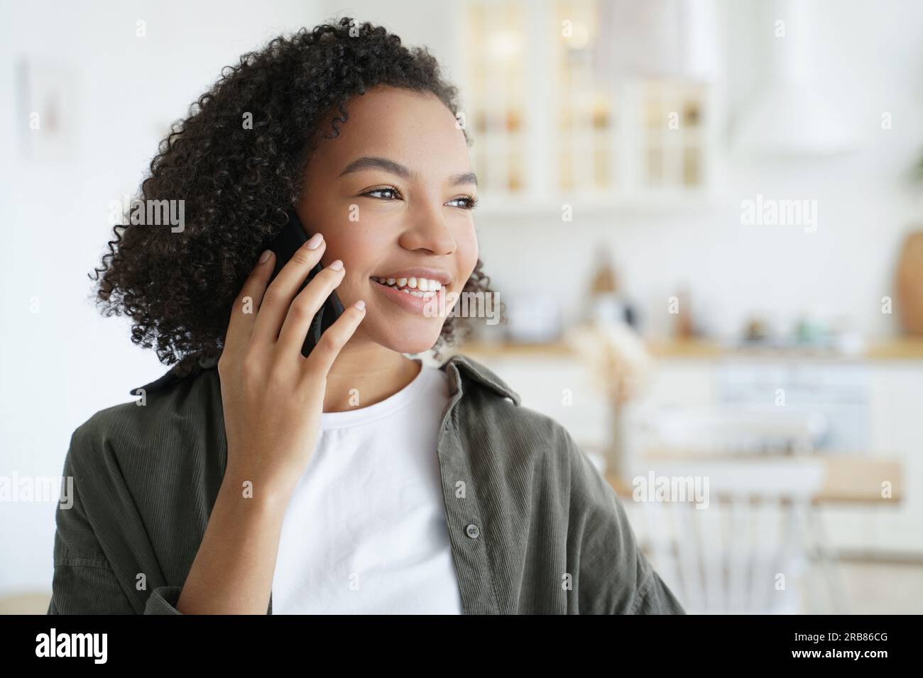 Smiling girl enjoys pleasant phone call at home. Biracial teen gets good news, chats happily on smartphone. Stock Photo