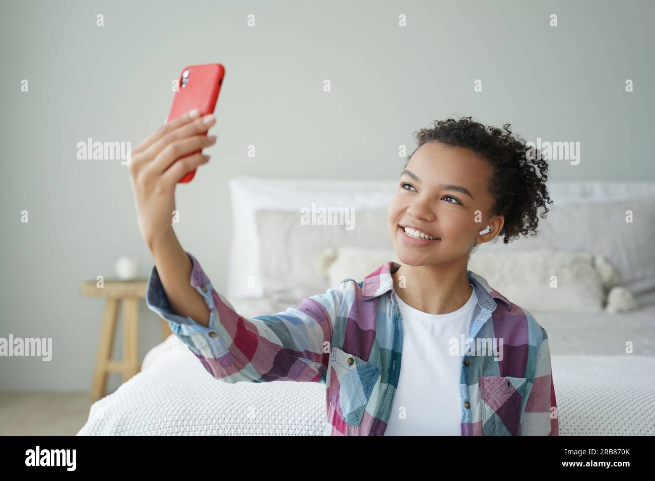 Biracial teen blogger chats online via phone video call, uses modern apps at home. Smiling girl takes selfie with smartphone. Stock Photo
