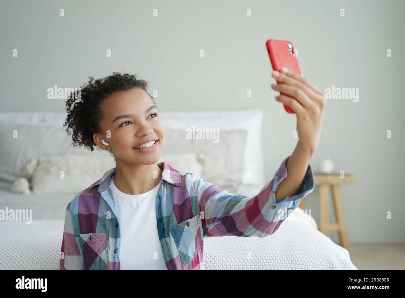 Biracial teen blogger chats online via phone video call, uses modern apps at home. Smiling girl takes selfie with smartphone. Stock Photo