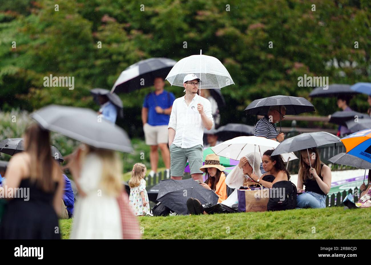 Spectators take shelter during a rain delay on day six