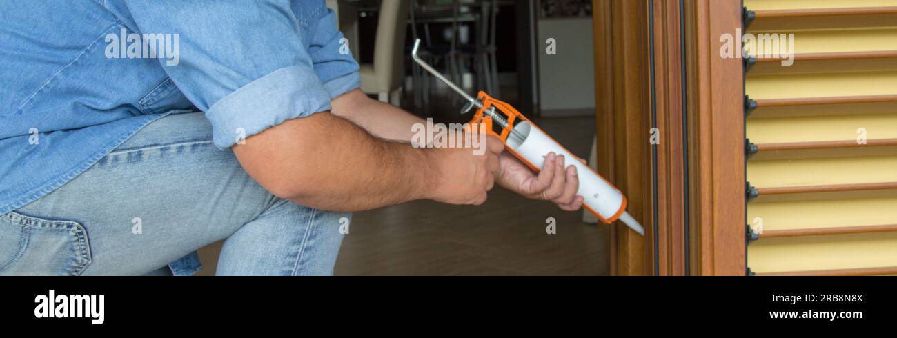 Image of the hands of a handyman who with a silicone gun installs and seals doors and windows against drafts. Home thermal insulation improvements. Stock Photo