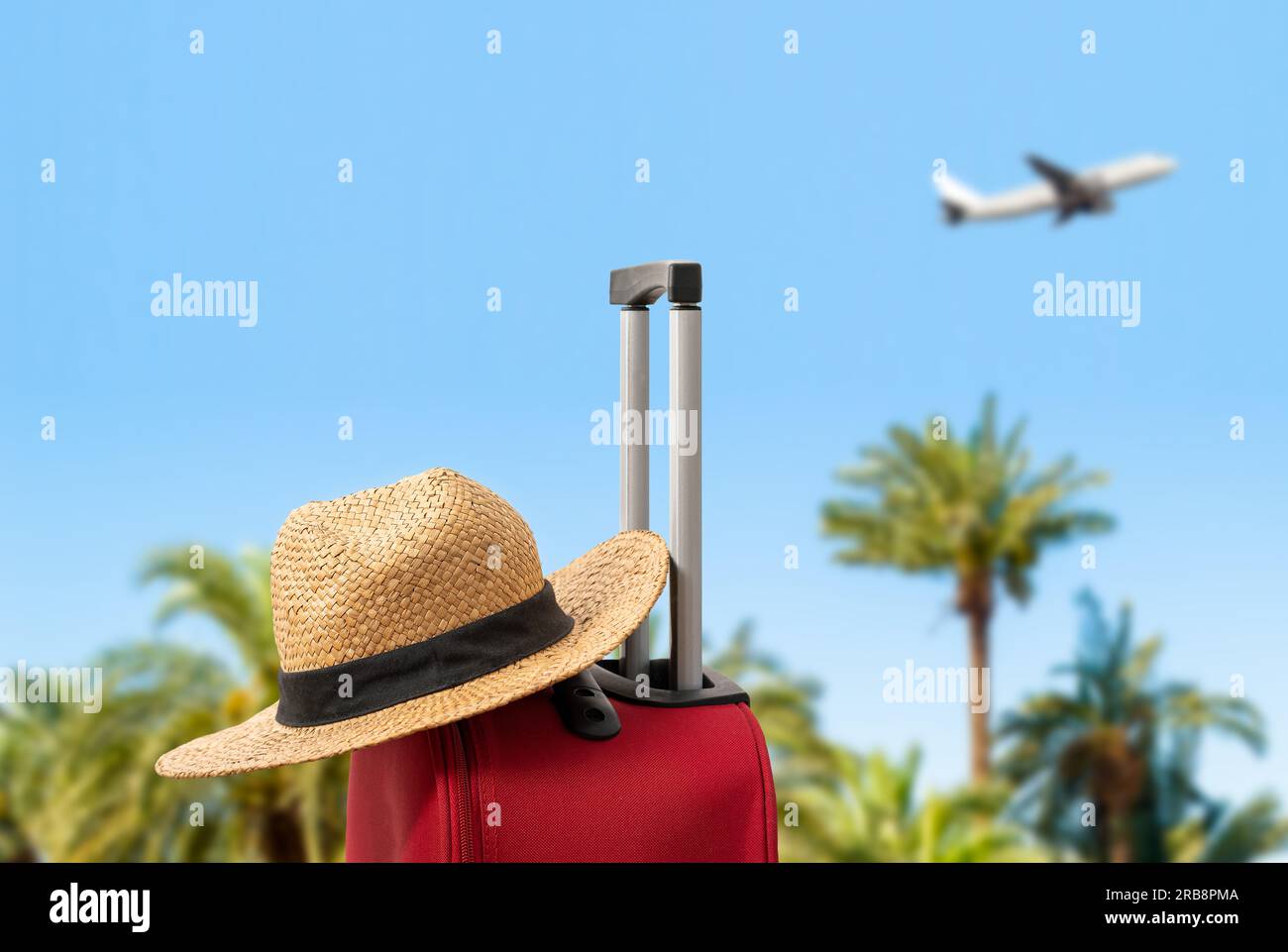 For travel and vacations purposes, a simple modern suitcase in red color at sea with palm trees and hat. Stock Photo