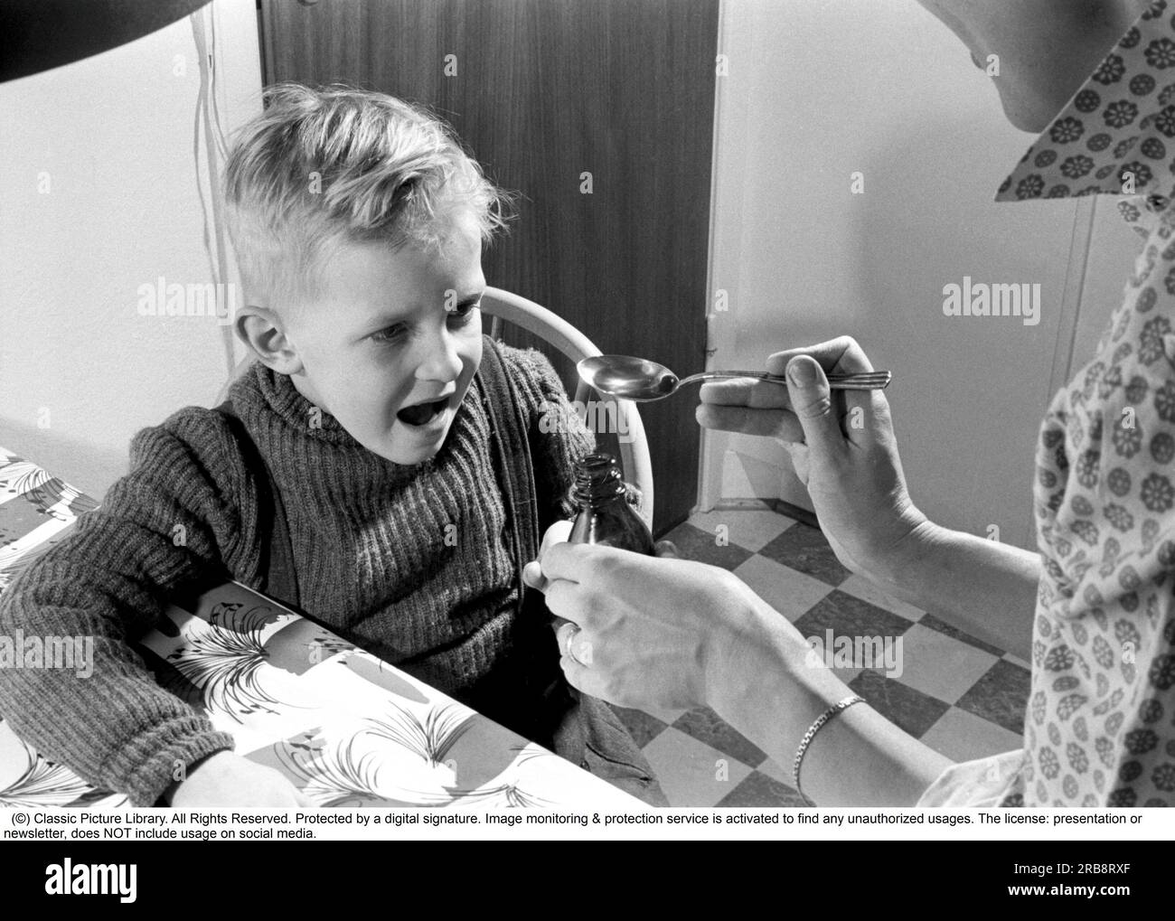 A boy is sick and won't take his medicine. His mother holds out a spoon