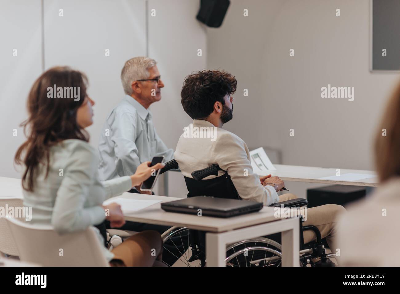 Handicapped employee in wheelchair listening to business lecture along ...