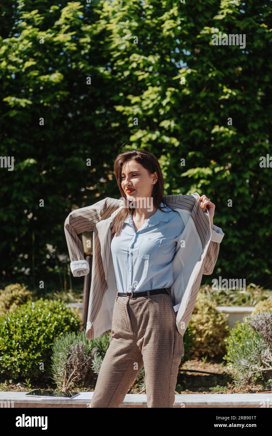 Smiley businesswoman putting a suit on after the wind started blowing early in the morning Stock Photo