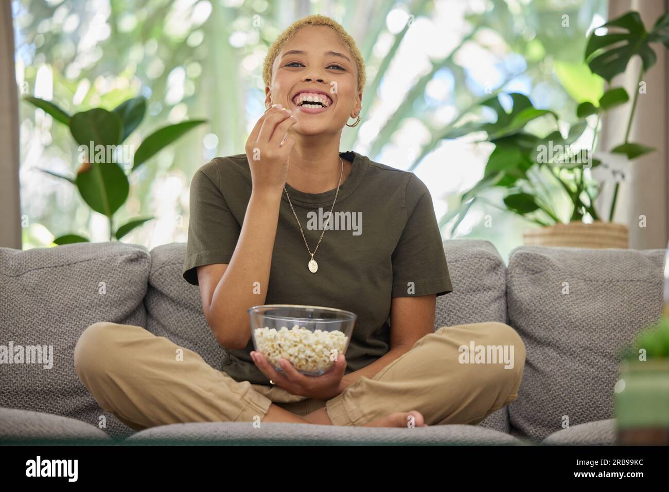 Woman on couch, popcorn and watch a movie with comedy and entertainment, streaming service and relax at home. Female person, subscription and internet Stock Photo