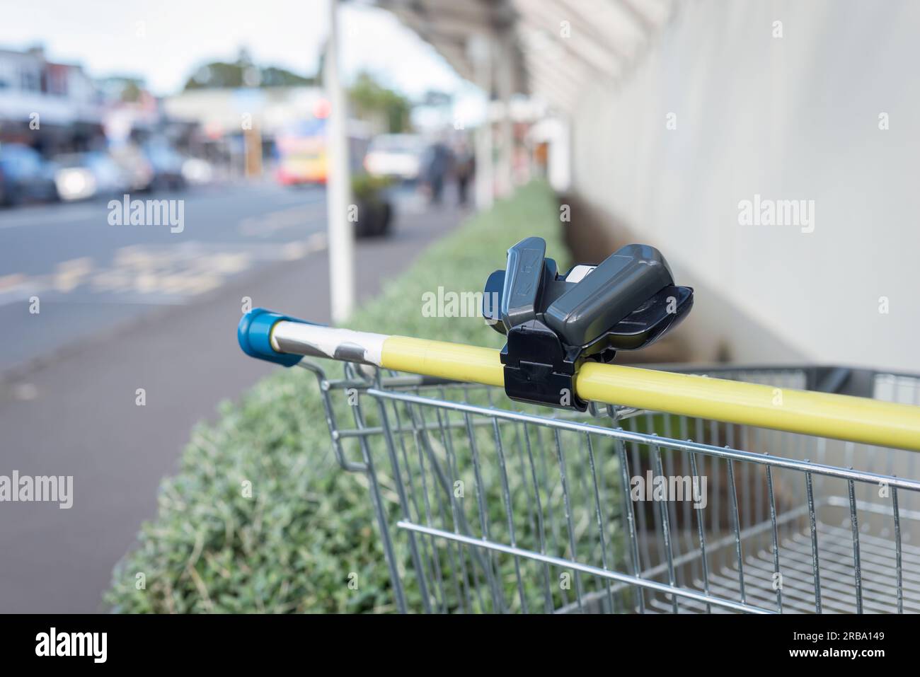 Supermarket trolley with smartphone holder on the handle bar dumped outside shopping mall. Out-of-focus bus and pedestrians on the road. Auckland. Stock Photo