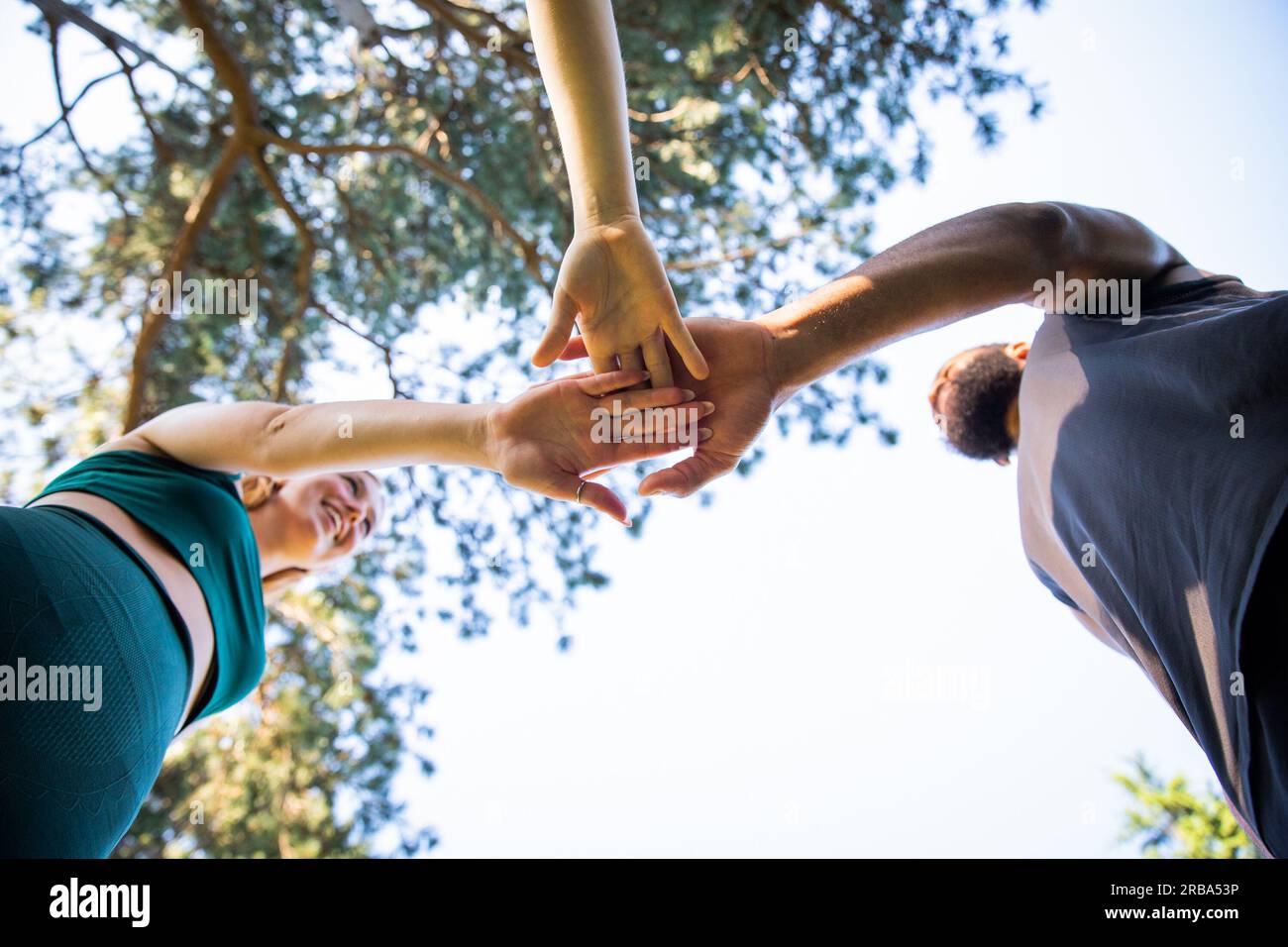 Three sportspeople join hands on top of each other, photo from below Stock Photo