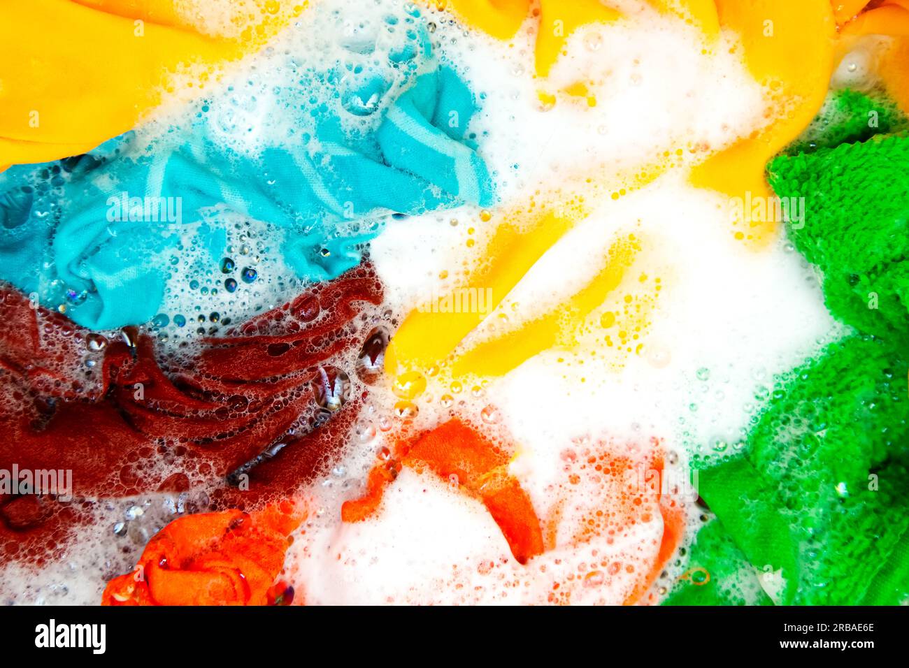 Colored clothes soaked in water with detergent and foam bubbles