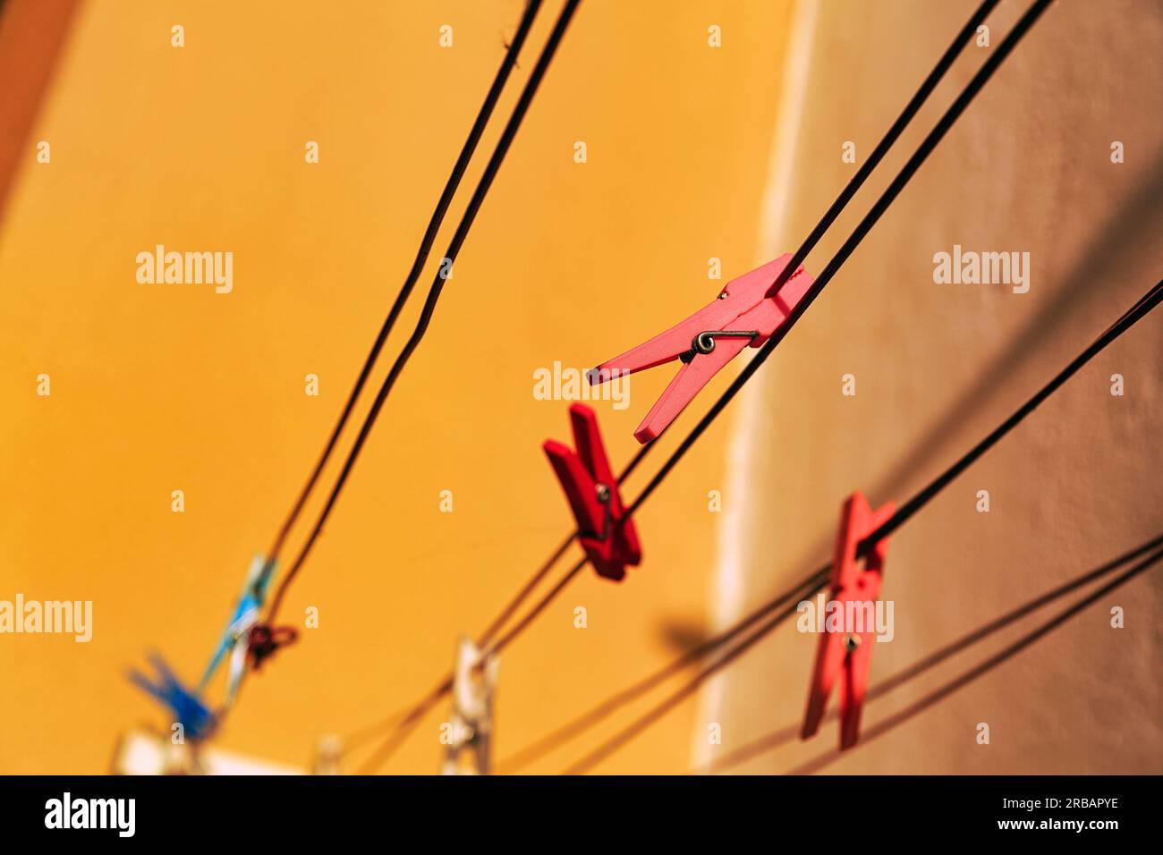 Red clothes pegs, empty clotheslines in front of orange house wall, colourful detail, Portugal Stock Photo