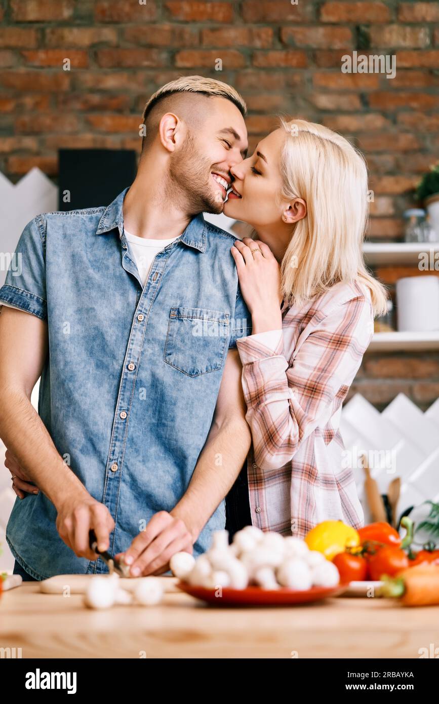 Young couple kissing and cooking together vegetarian meal in the kitchen at home. Healthy happy lifestyle concept Stock Photo