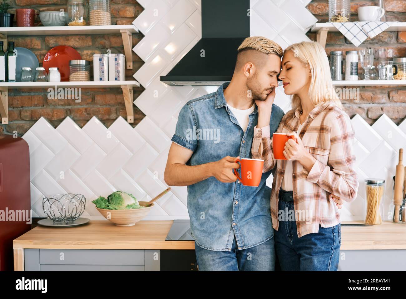 Young happy couple in love drink coffee in the morning embracing in kitchen at home. Relationship, family concept Stock Photo