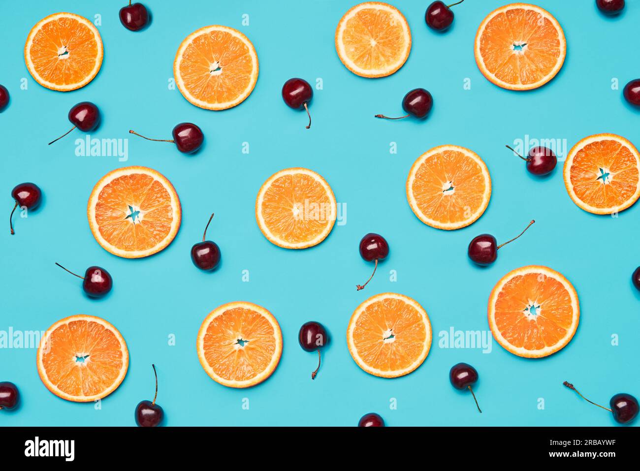 Orange slices and sweet cherries on blue background. Food wallpaper, summer, vgetarian concept Stock Photo
