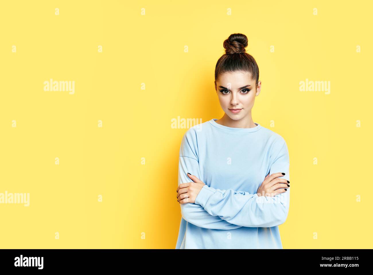 Pretty confident young beautiful woman in casual clothing with crossed arms looking at camera over yellow background Stock Photo