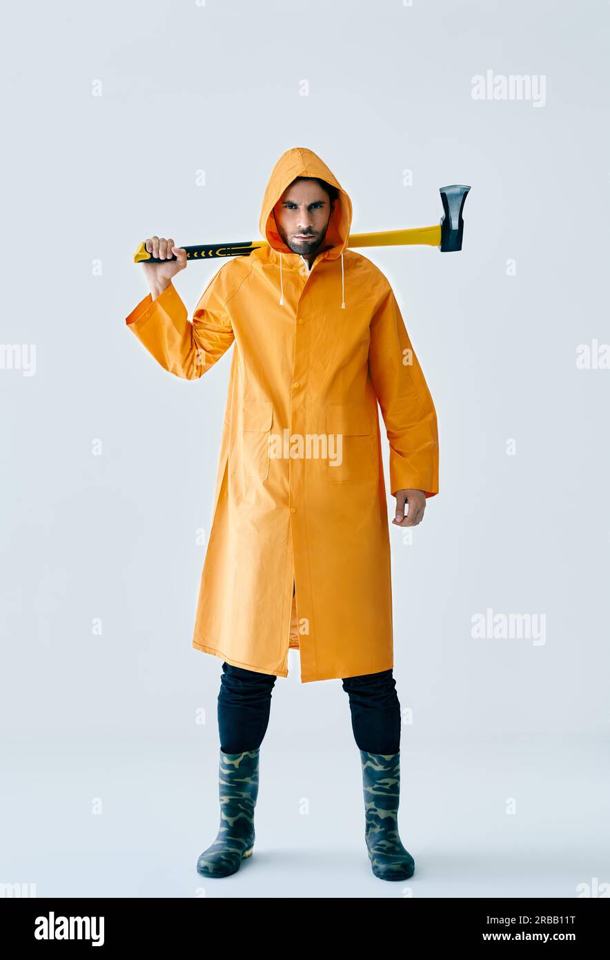 Full length portrait of young handsome man in bright raincoat holding big axe. Brutal male, lumberjack, fisherman with ax Stock Photo