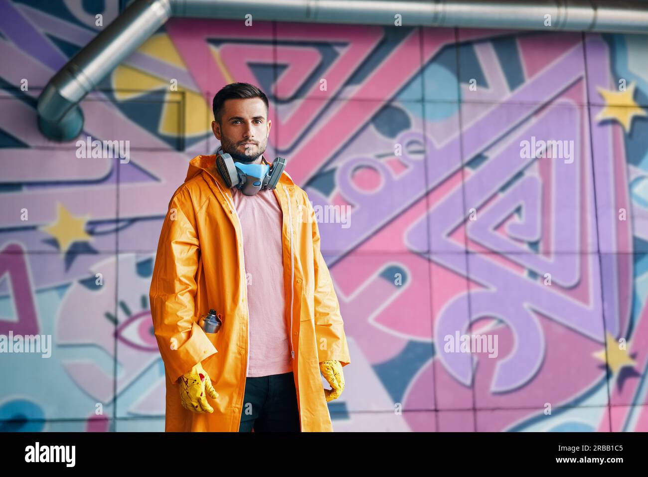 Young graffiti painter standing near the wall with his paintings with