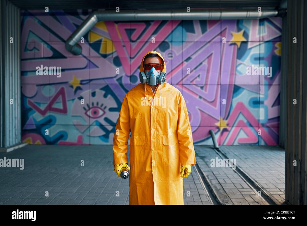 Graffiti painter in respirator mask standing near the wall with his