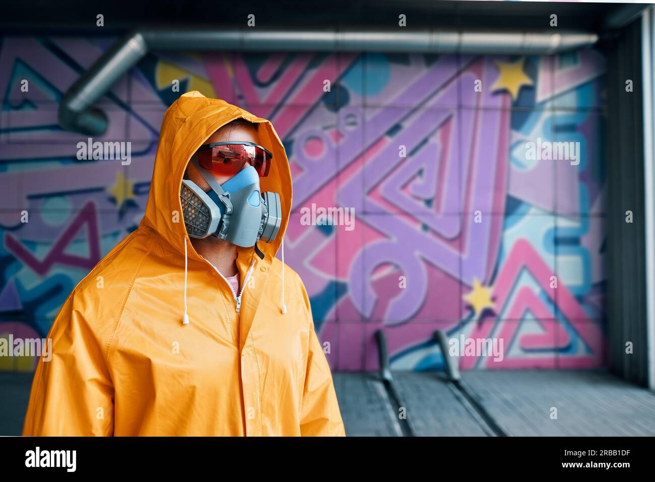 Graffiti painter in respirator mask standing near the wall with his