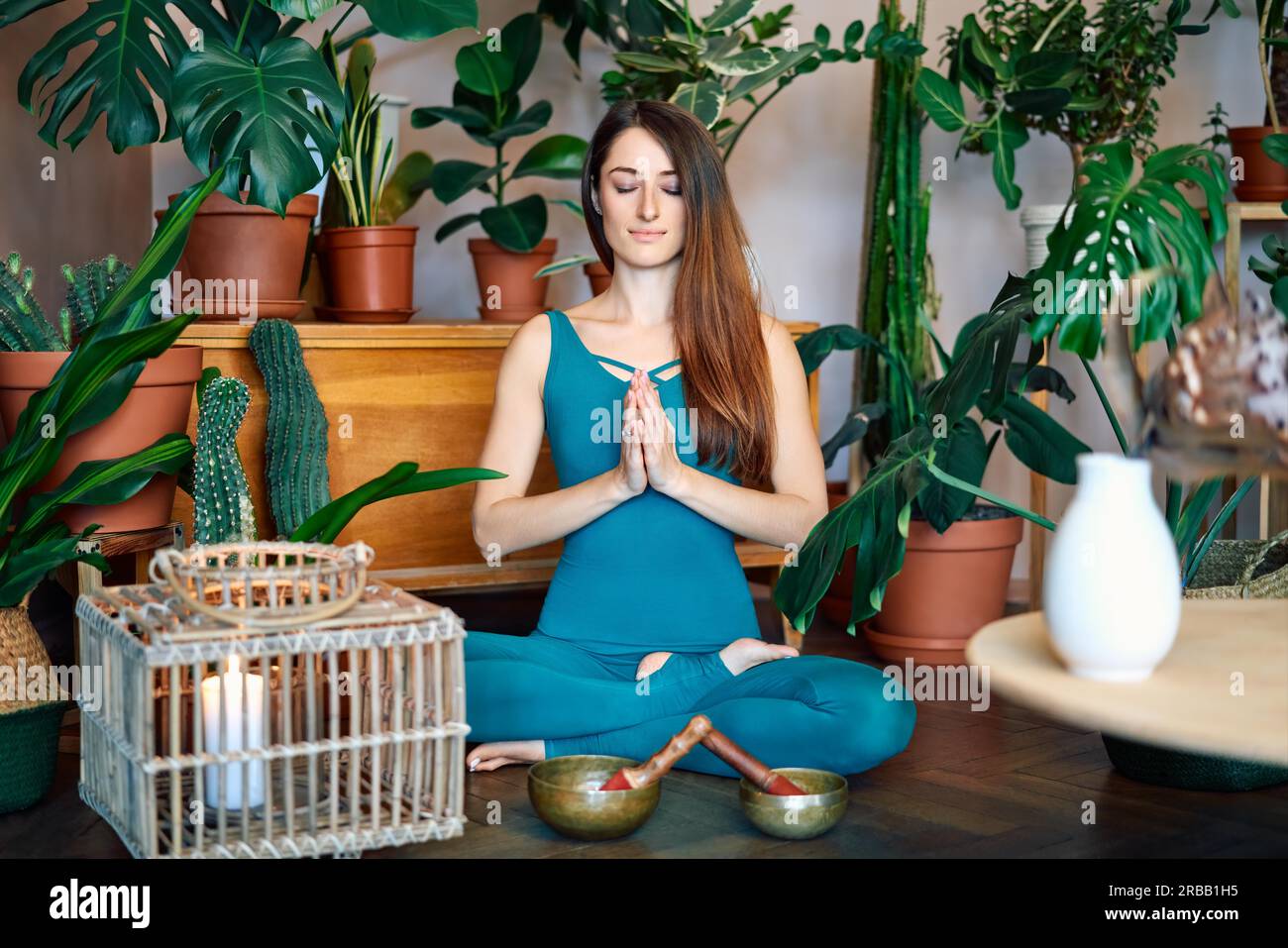 Young woman practicing yoga doing Ardha Padmasana exercise with namaste at home. Lotus pose, meditation concept Stock Photo