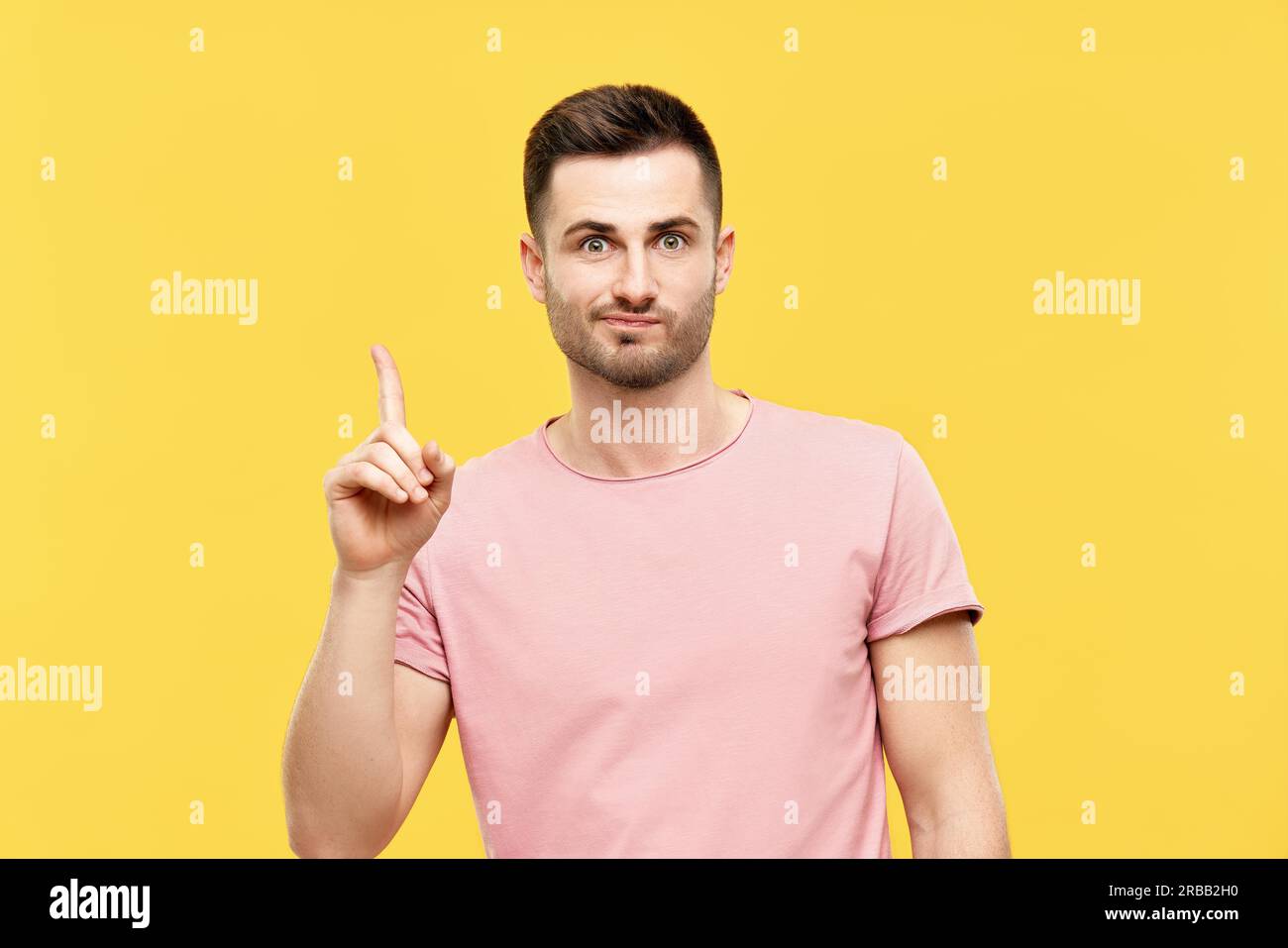 Young funny man pointing his finger up indicates to copy space isolated on yellow background. Presenting product and advertising concept Stock Photo