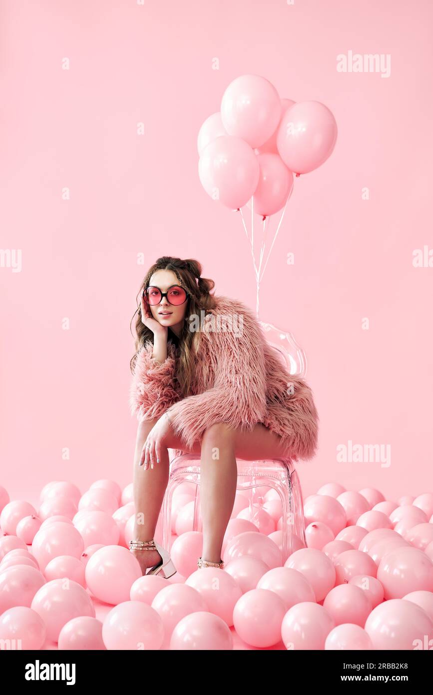 Confident fashion woman sitting on chair posing on many pink