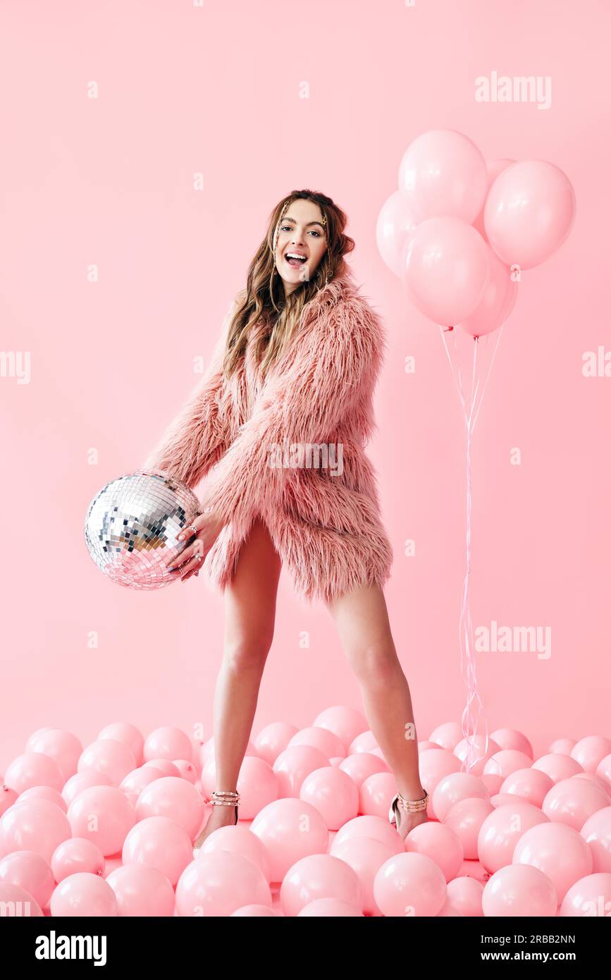 Trendy young woman have fun with party disco ball on pink balloons background. Emotions, celebrate concept Stock Photo