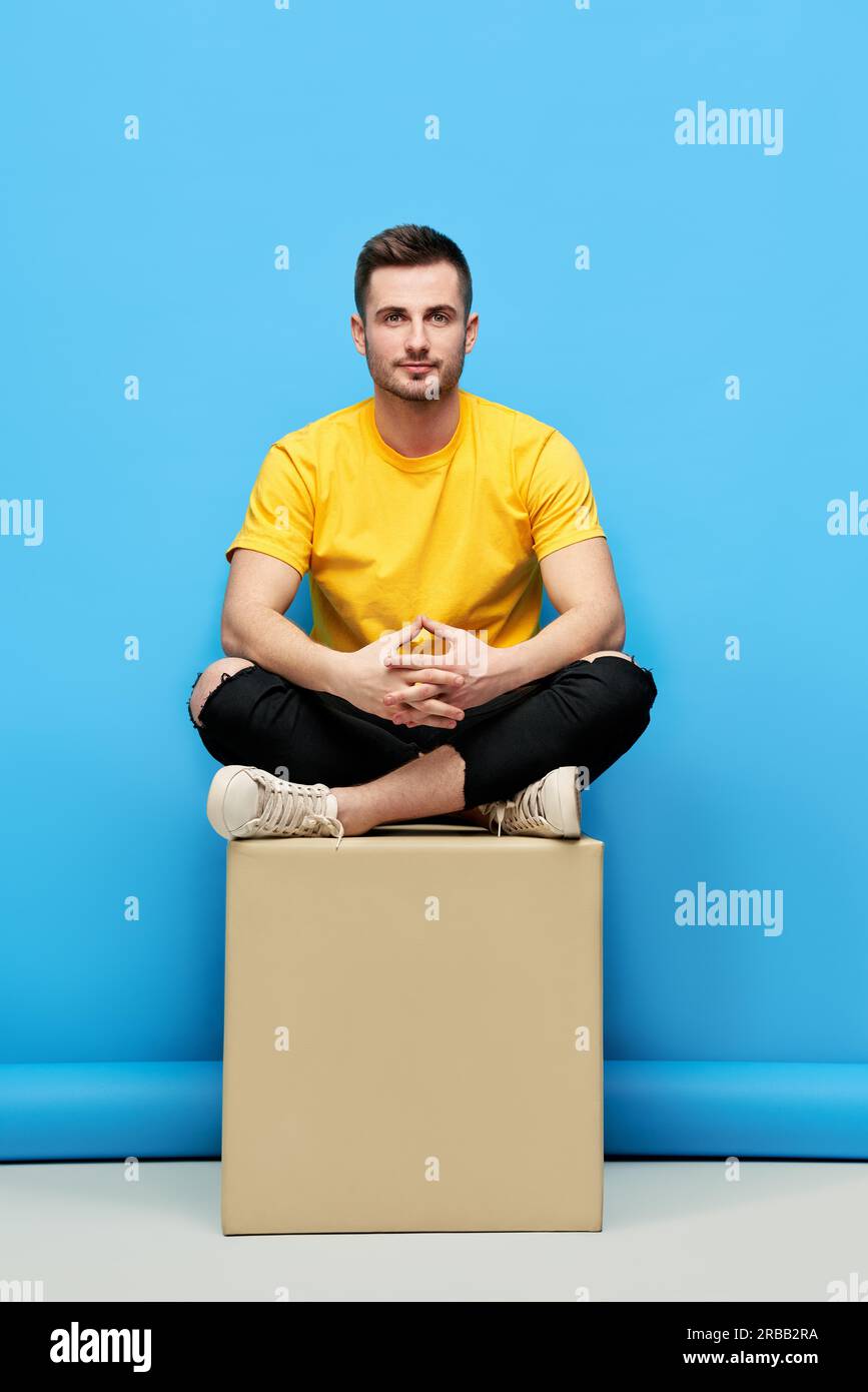 Handsome hipster man sitting on cube at studio. Mens beauty Stock Photo