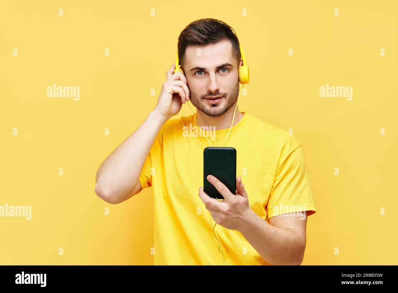 Handsome caucasian man listening to music from his phone and headphones over yellow background Stock Photo