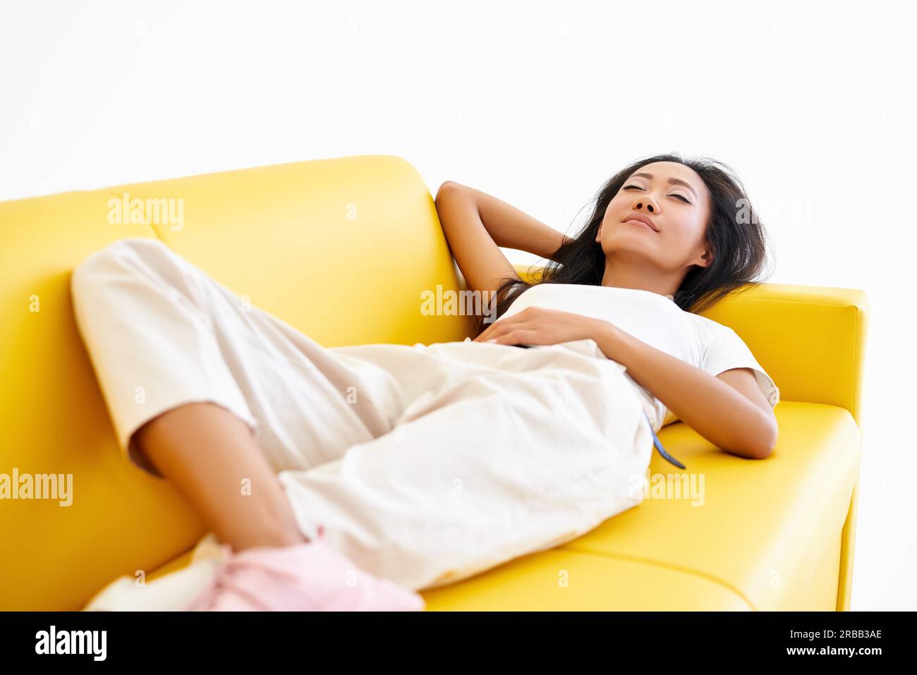 Young pretty woman closed her eyes lying on yellow sofa and relaxing ...