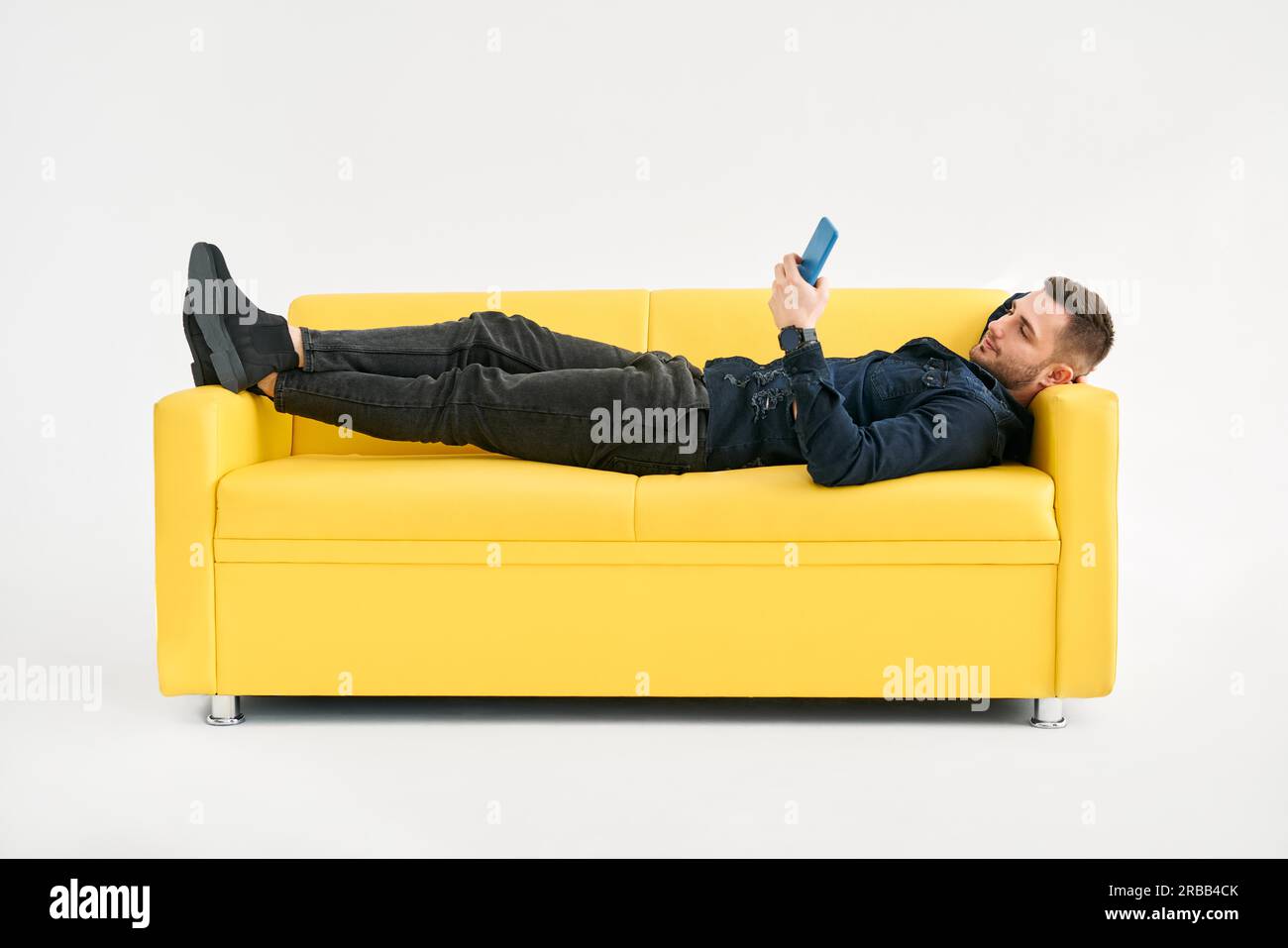 Relaxed man lying on yellow sofa using smartphone over white background Stock Photo