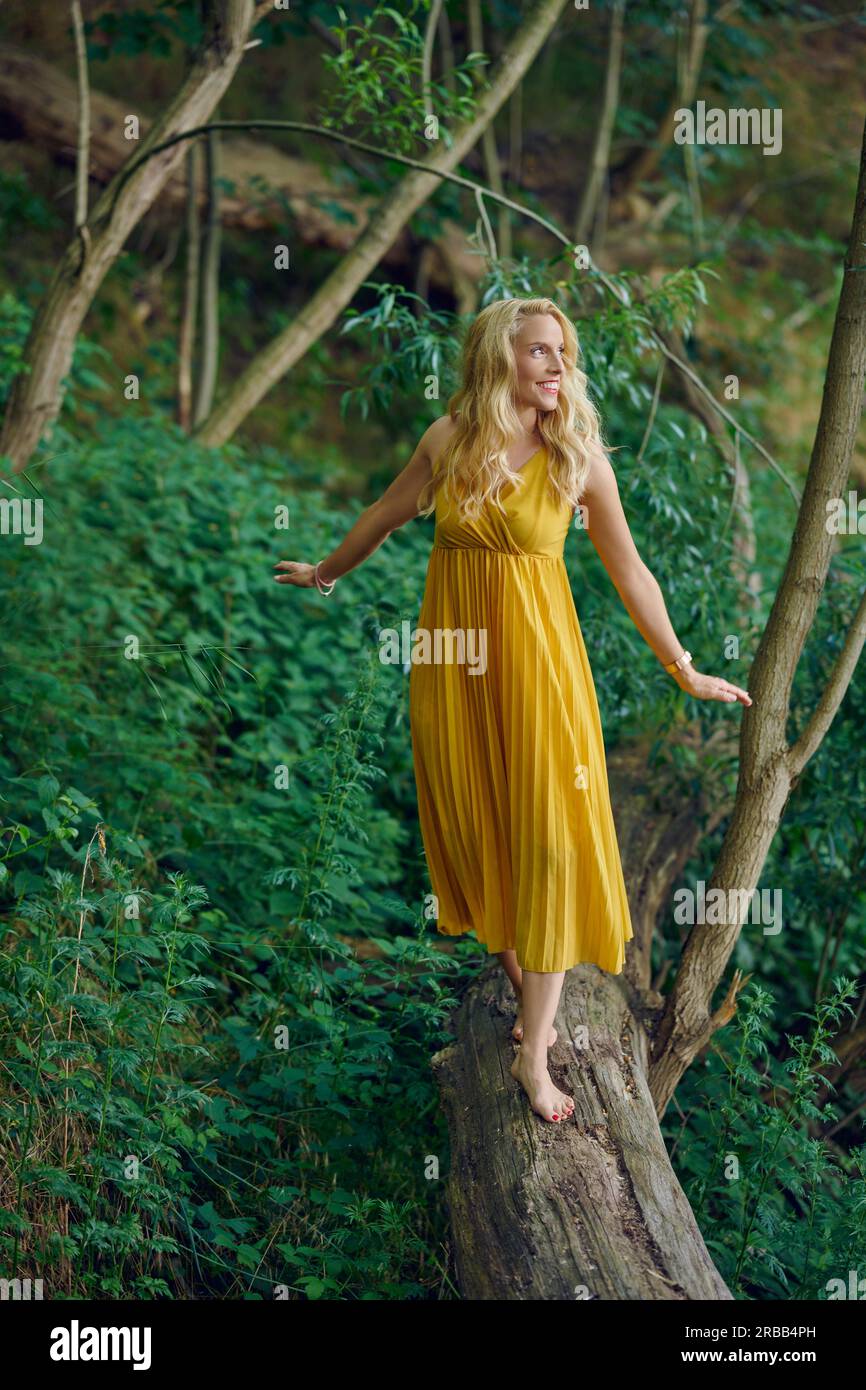 Carefree barefoot attractive blond woman balancing on an old fallen log in  a forest wearing an elegant yellow dress looking away to the side with a  Stock Photo - Alamy