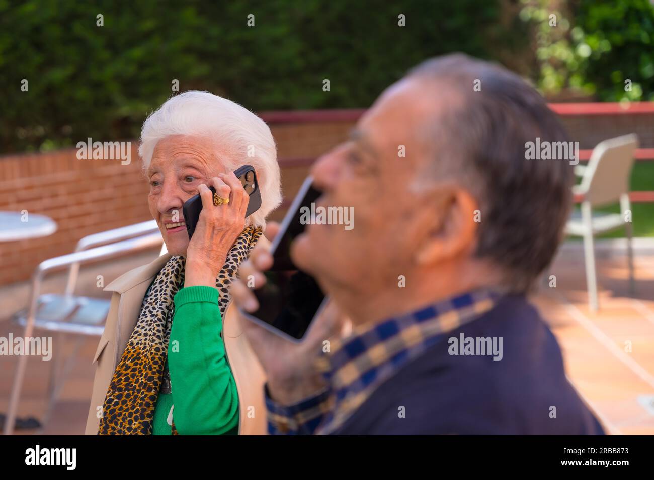 Two elderly people in the garden of a geriatric retirement home, talking on the phone, technologies in the elderly Stock Photo