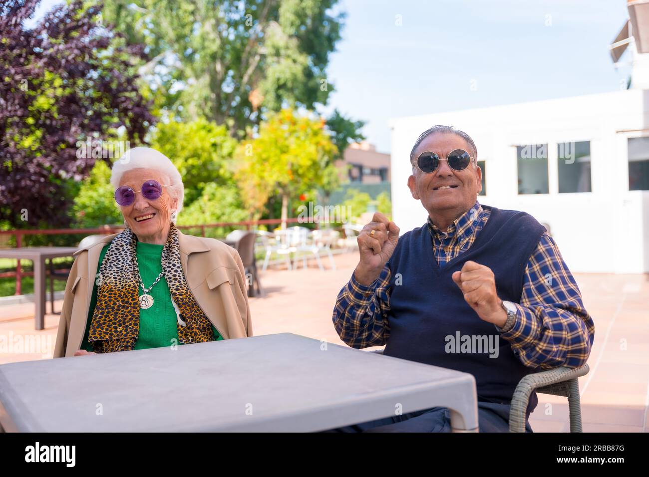 Two seniors dancing in the garden of a nursing home or retirement home at a summer party wearing sunglasses Stock Photo